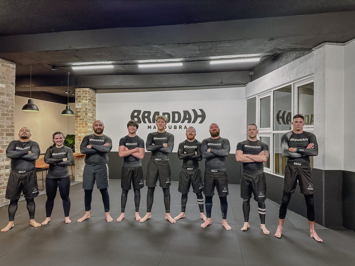 Braddah Jiu Jitsu Maroubra instructors standing together on the training mats in branded rash guards and shorts inside the academy.