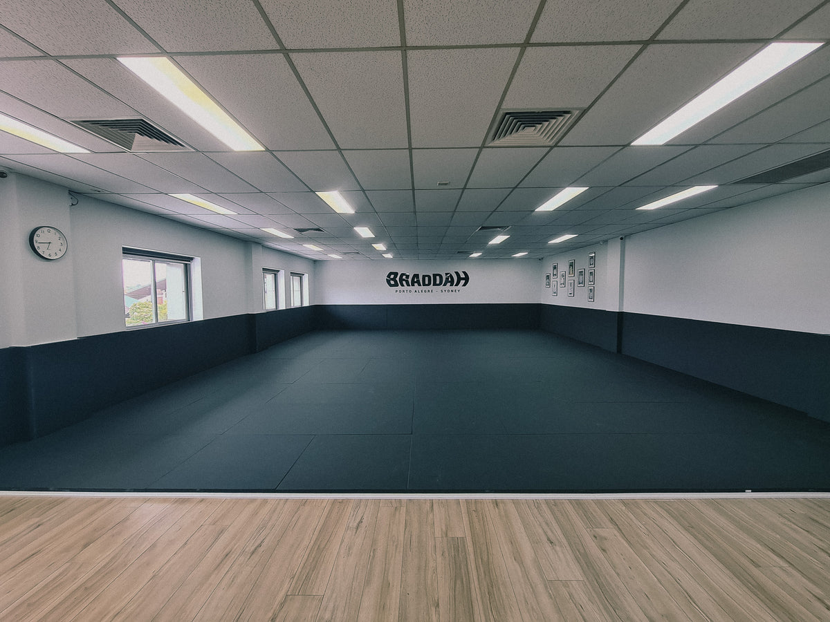Braddah Jiu Jitsu training facility featuring a spacious matted area, black wall padding, and Braddah branding on the back wall.