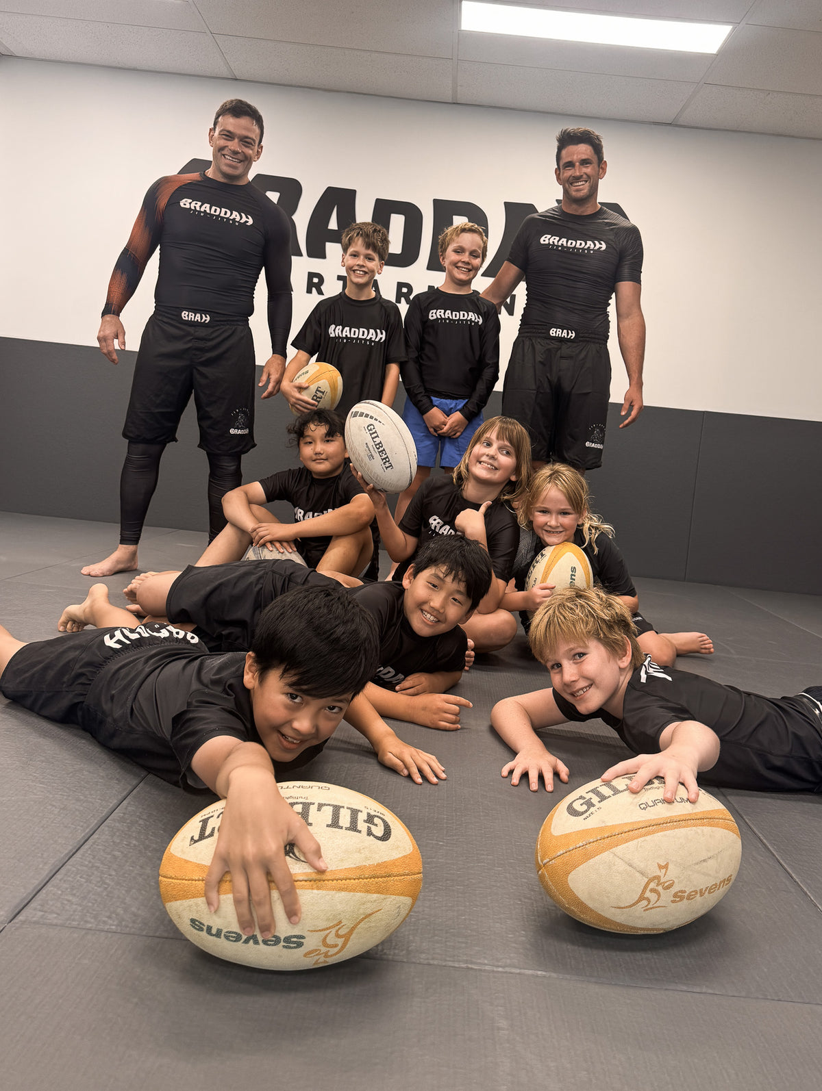 Braddah Jiu-Jitsu Artarmon coaches and children posing with rugby balls during a kids training session